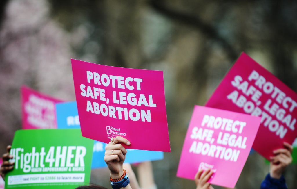 People hold up signs that read "Protect safe, legal abortion."